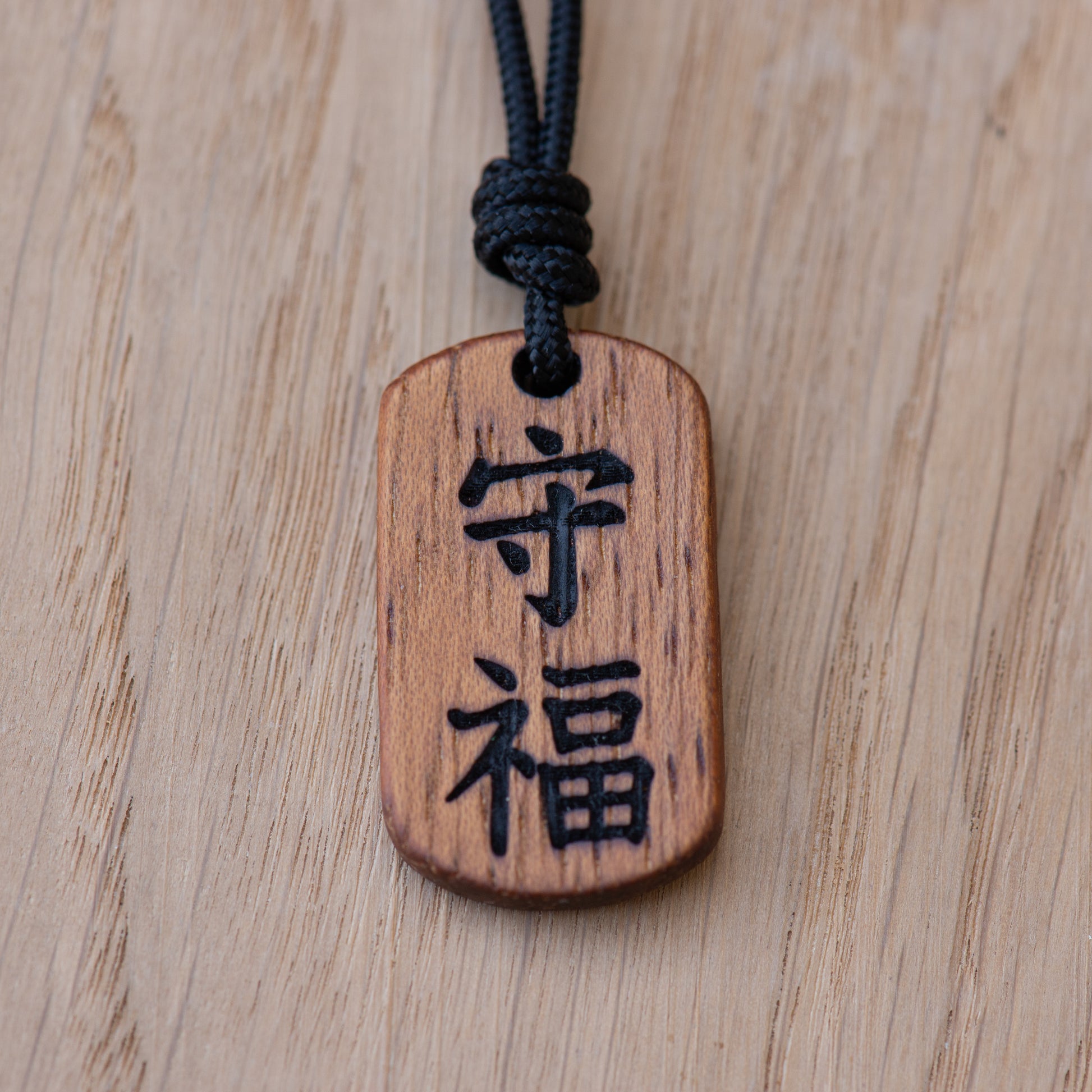 Close up of Mamoru and Fuku kanji engraving on solid Iroko wood pendant